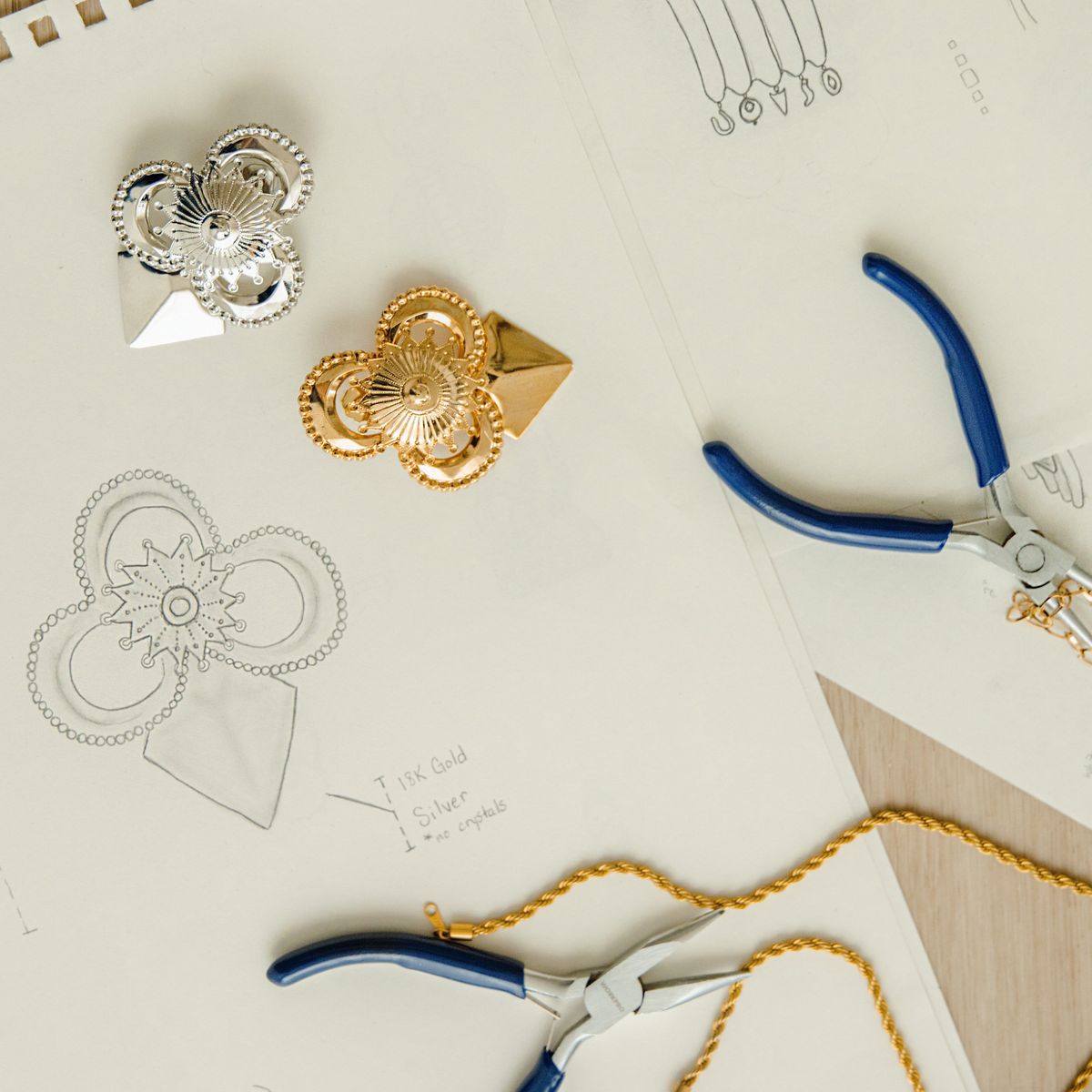Geometric stud earrings with intricate detail, and a pointed triangular base on sketching pad.