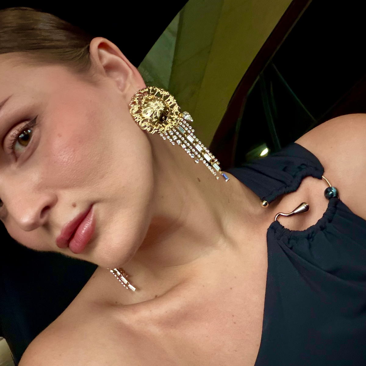 A close-up lifestyle shot of a woman wearing a dramatic gold filigree detailed statement earring with cascading Swarovski crystal fringe.