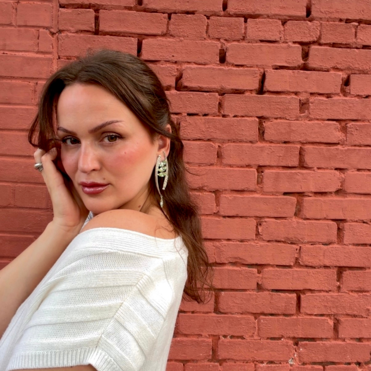 A woman posing against a red brick wall, wearing a pair of silver-toned crescent-shaped drop earrings featuring marquise-cut mint green Swarovski crystals and ornate filigree details.